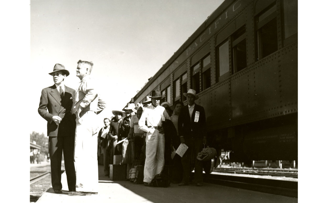 A photo of officials standing with a group of braceros by a Southern Pacific train in California, 1942..png